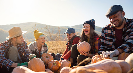 Diverse group of four students wearing fall attire and laughing while sitting in a pumpkin patch