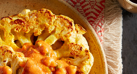 Image of Grilled Cauliflower Tikka Masala on a beige plate with red and cream colored tasseled placemat.