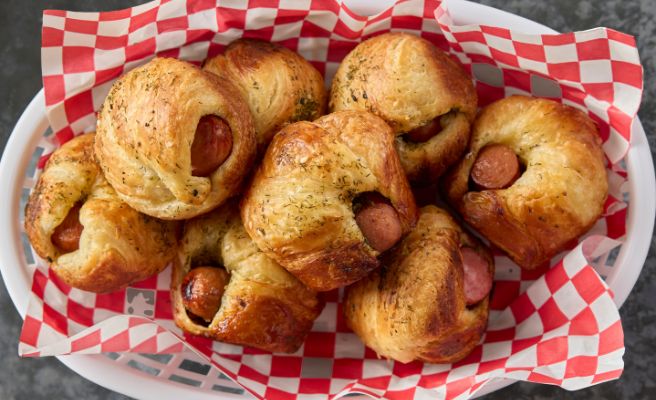 Plastic basket lined with paper filled with multiple Hot Dog Cruffins.