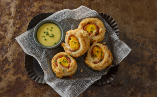 Four Biscuit Benedict Dippers on a lined tray with a side of hollandaise curry sauce in a small cup garnished with chives.