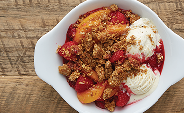 Triple Berry Granola Crisp in white bowl on wooded surface