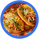 Two delicious tacos topped with lettuce, cheese, tomatoes, and sour cream on a decorative plate against a bright blue background.