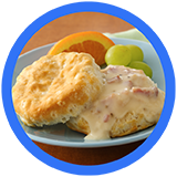 Flaky biscuit smothered in creamy sausage gravy, served with grapes and an orange slice on a blue plate.