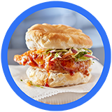 A crispy fried chicken sandwich layered with fresh greens and spicy sauce, nestled between a soft, flaky biscuit.