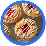 Five cherry-topped pastries drizzled with white icing and sprinkled with almond slivers, resting on a wire rack.